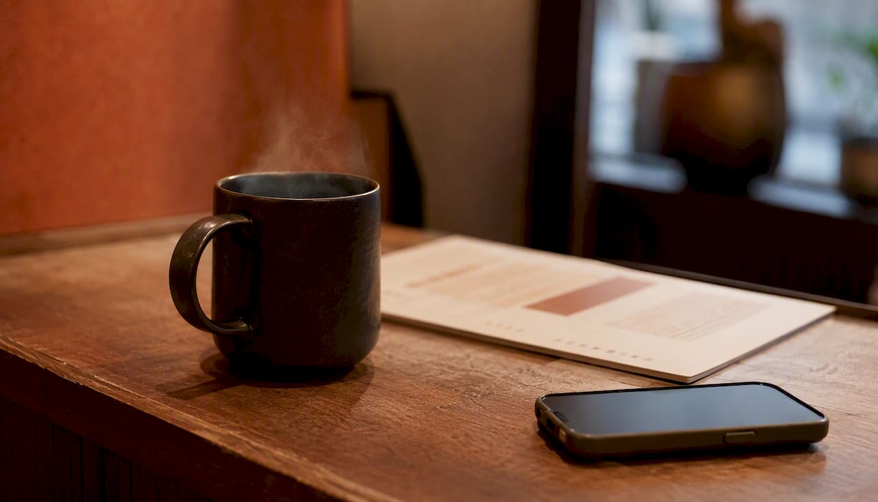 Taza de café en el mostrador de recepción con un guion telefónico bilingüe y un teléfono